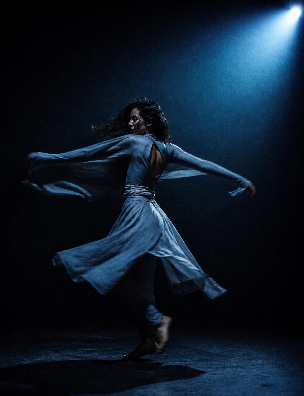 Contemporary dancer spinning under a cool blue spotlight