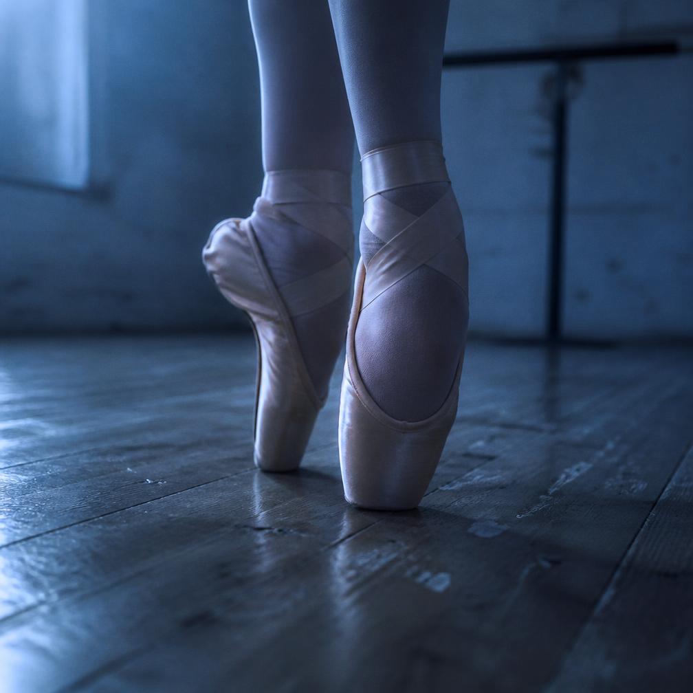 Close view of a ballet dancer's feet en pointe on a wooden floor
